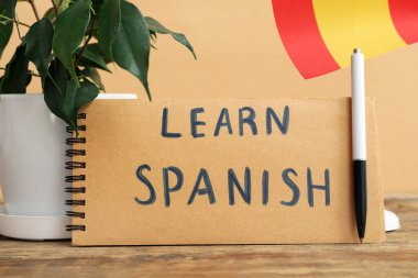 Bej arkaplana karşı masada Learn SPANISH, kalem, çiçek ve bayrak içeren defter