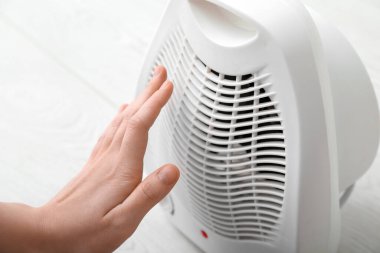 Evdeki elektrikli fan ısıtıcısının yanında ısınan kadın, yakın çekim.