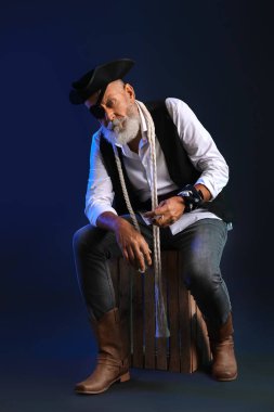 Karanlık arka planda oturan ip ve kutulu yaşlı korsan.