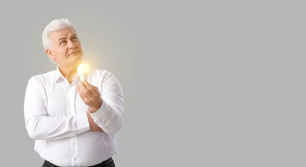 Thoughtful senior businessman with light bulb on grey background. Concept of idea