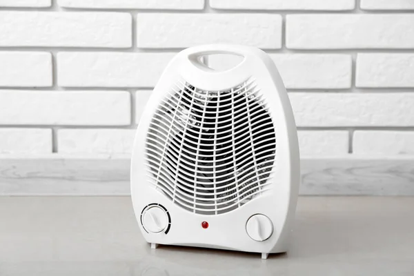 Electric fan heater near white brick wall