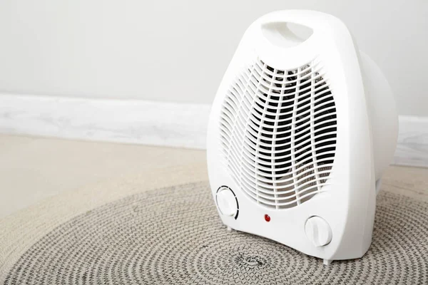 Electric fan heater on rug near light wall