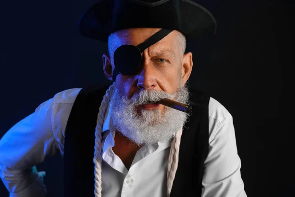 Old pirate with cigarette on dark background, closeup