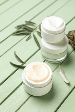 Yeşil ahşap arka planda zeytin dalı olan krema kavanozları, yakın plan.