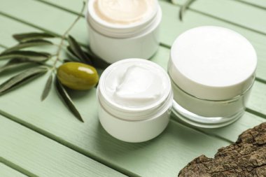 Bitki dallı krema kavanozları, yeşil ahşap arka planda zeytin ve ağaç kabuğu, yakın plan.