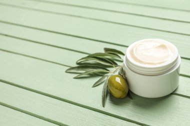 Yeşil ahşap arka planda zeytin ve bitki dallı bir kavanoz krema.