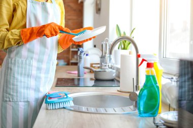 Young woman cleaning plate with brush in kitchen