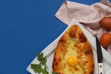 Mavi arka planda lezzetli Ajarian Khachapuri tabağı, yakın plan.