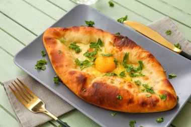 Renkli ahşap arka planda lezzetli Ajarian Khachapuri tabağı, yakın plan.
