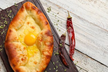 Lezzetli Ajarian Khachapuri ve hafif ahşap arka planda kuru kırmızı biberli pano, yakın plan.