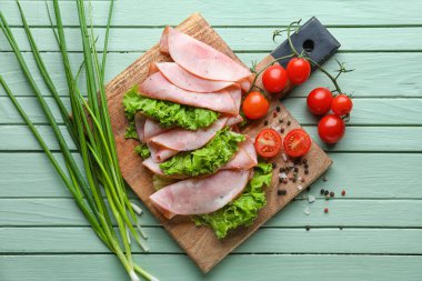 Lezzetli jambon, marul, domates ve ahşap arkaplanda yeşil soğan dilimleri.