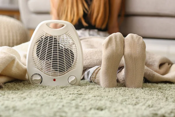 Electric fan heater and woman in warm socks at home, closeup