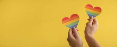 Sarı arkaplanda gökkuşağı kalplerini tutan kadın elleri ve metin için boşluk. LGBT kavramı