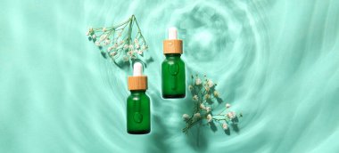 Kozmetik serumu şişeleri ve yeşil arka planda sudaki çiçekler.