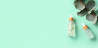 Kozmetik serumu şişeleri ve turkuaz arka planda okaliptüs dalı metin için alan, üst görünüm