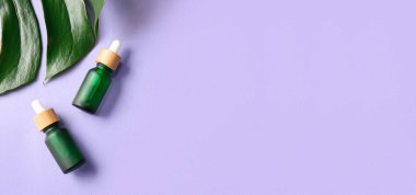 Kozmetik serumu şişeleri ve eflatun arkaplan üzerinde tropikal yaprak metin için alan, üst görünüm