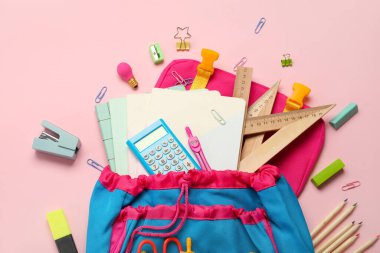 School backpack with stationery supplies on pink background