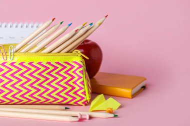 Case with pencils, paper plane, apple and calendar on pink background