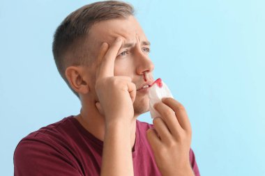 Burnu kanayan ve mavi arka planda dokusu olan genç adam, yakın plan.