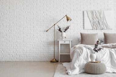 Masa, lamba ve vazolarda okaliptüs dallarıyla aydınlık yatak odasının içi.