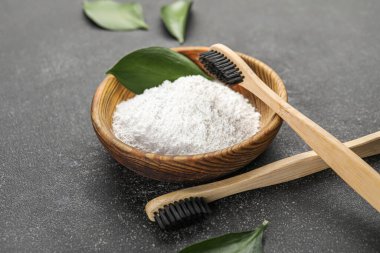 Koyu arkaplanda diş fırçası ve yaprakları olan bir kase diş tozu.