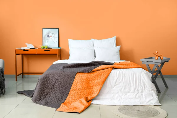 Big bed with soft linen and tables near orange wall in room