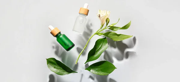 Bottles of cosmetic serum and leaves on light background, top view