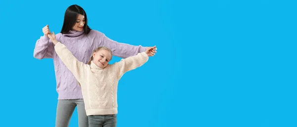 幸せな母親と彼女の小さな娘で暖かいですセーターダンスで青背景とともにスペースのためにテキスト — ストック写真