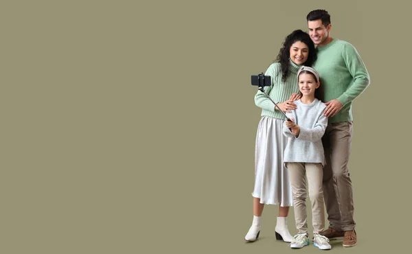 Happy family in warm sweaters taking selfie on color background with space for text