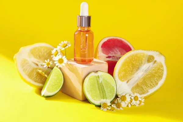 Composition with bottle of essential oil, citrus fruits and chamomile flowers on yellow background