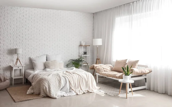 Interior of light bedroom with lamps, tables and couch