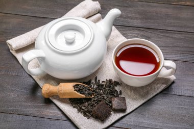 Koyu ahşap arka planda bir kepçe kuru çay, fincan ve çaydanlık ile peçete