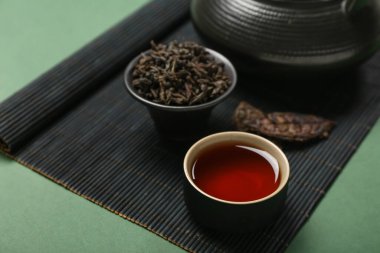 Bir kase kuru puer çaylı bambu, yeşil arka planda fincan ve demlik, yakın plan.