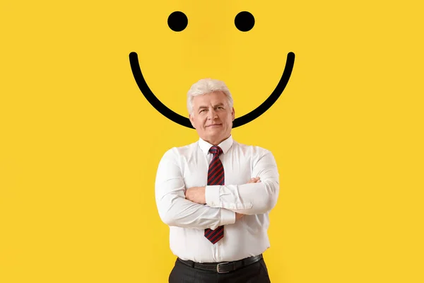 Stylish mature businessman and drawn smile on yellow background