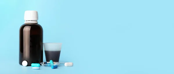 Bottle and cup of cough syrup with pills on blue background. Banner for design