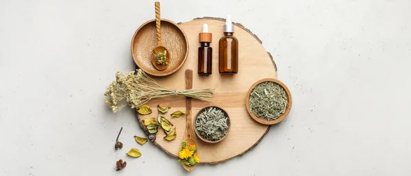 Composition with different dry herbs and bottles of essential oil on light background, top view