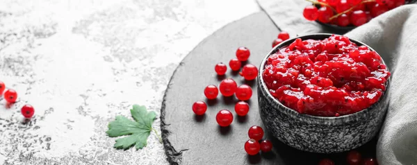 Bowl with tasty red currant jam on grunge background, closeup