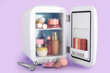 Leylak arka planında makyaj ürünleri olan kozmetik buzdolabı.