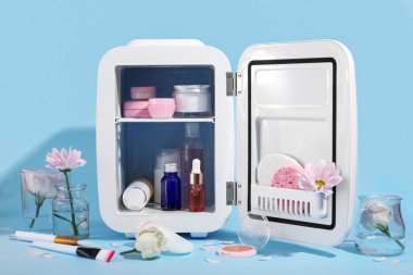 Mavi arka planda kozmetik ürünleri ve çiçekli küçük buzdolabı