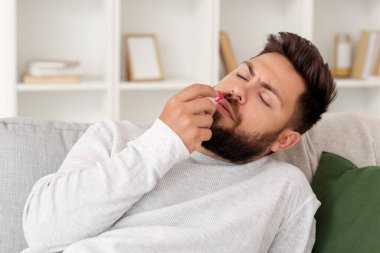 Evde burnu kanayan ve mendili olan sakallı genç bir adam.