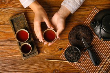 Ahşap arka planda bir fincan aromatik puer çaylı kadın elleri.
