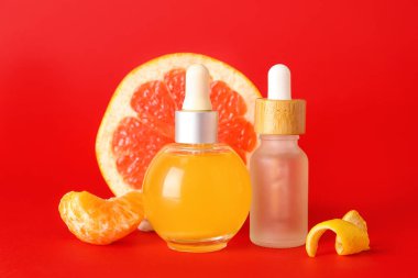 Kırmızı arka planda narenciye serumu şişeleri