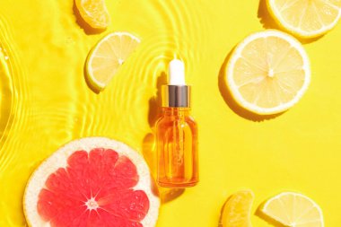 Bir şişe narenciye serumu ve sarı arka planda sudaki meyveler.