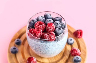 Pembe arka planda bir bardak puding ve böğürtlenli pano, yakın plan.