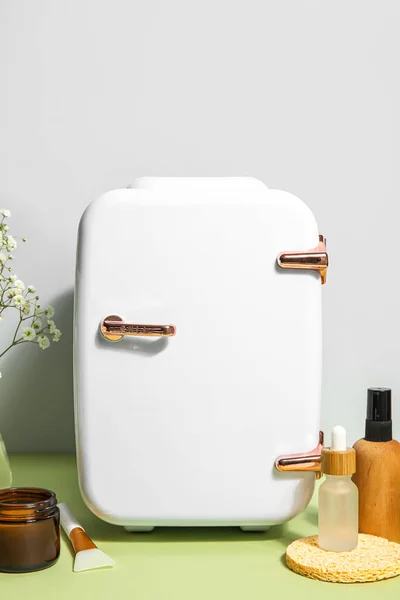 Small refrigerator with natural cosmetics on table near grey wall