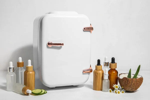 Small refrigerator with natural cosmetics and ingredients on white background