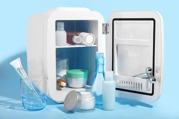 Small refrigerator with cosmetics on blue background