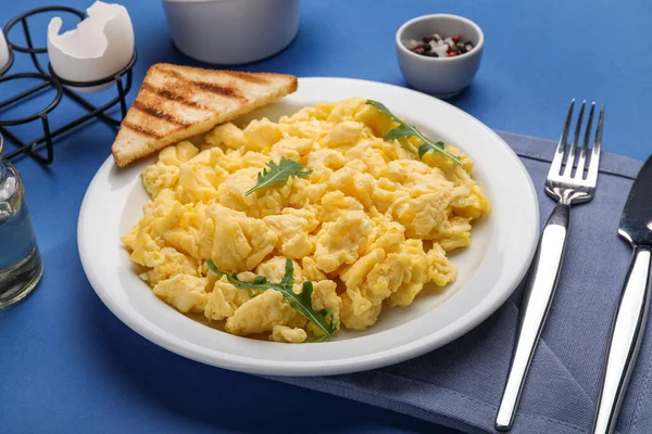 Plate of tasty scrambled eggs and toast on blue background, closeup
