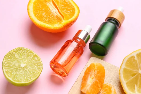 Composition with bottles of citrus serum and fruits on pink background, closeup