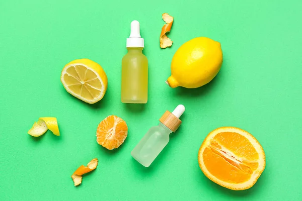 Composition with bottles of citrus serum and fruits on green background